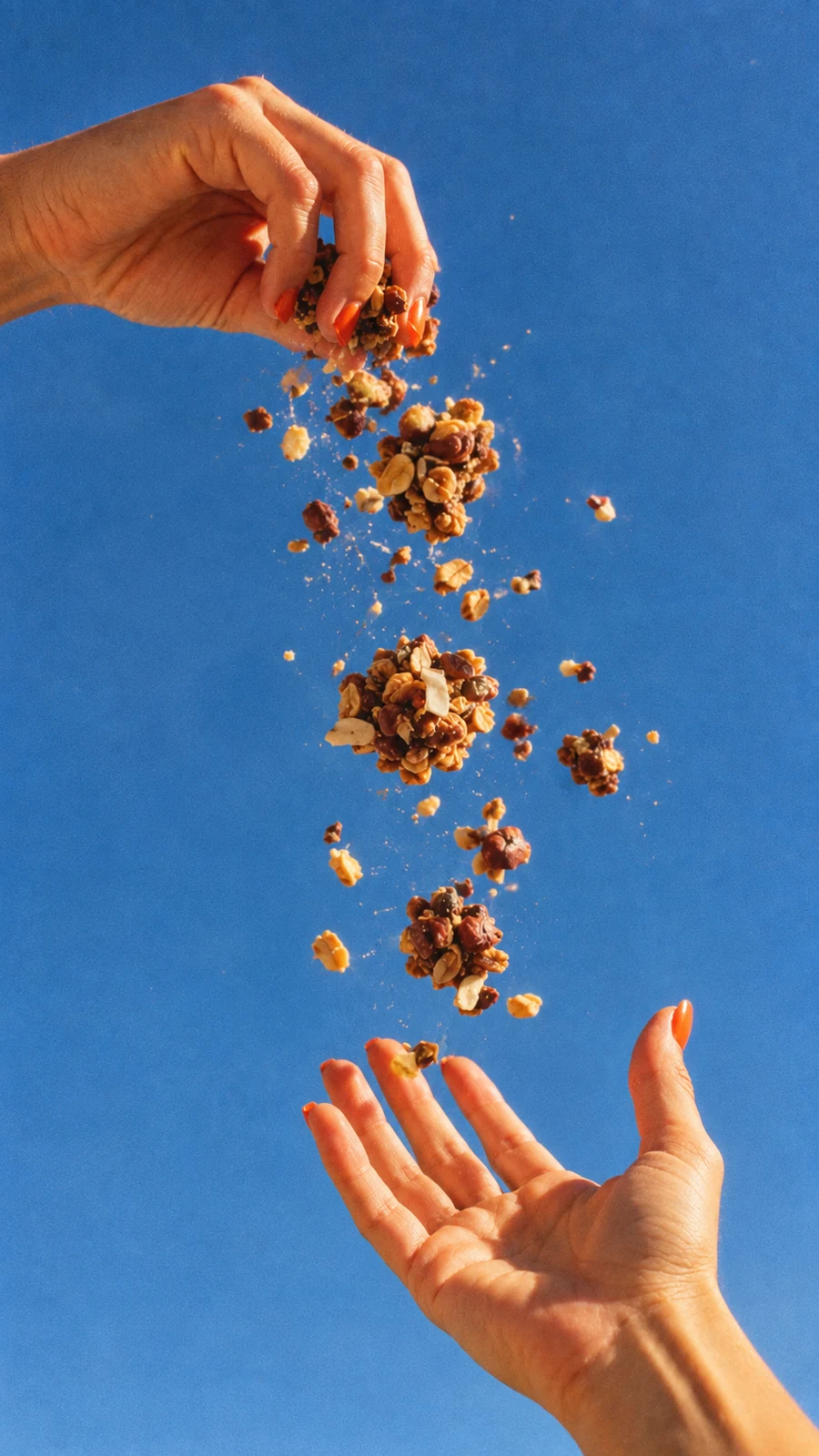 Granola en movimiento entre dos manos sobre un fondo azul